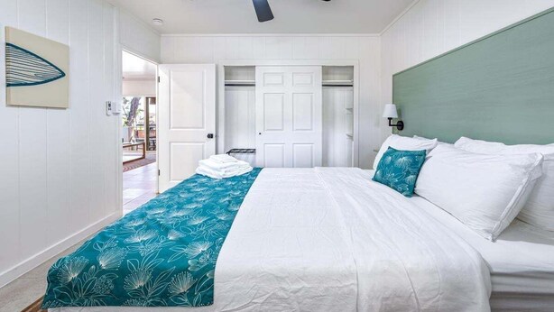 A bedroom with a bed, a ceiling fan, a green headboard, and a white door. - Big Island Kahaluu Surf Boutique #4 2 Bedroom Apts (Kailua-Kona)