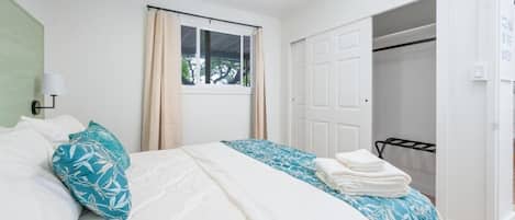 Ein Schlafzimmer mit Bett, einem Fenster mit Vorhängen, einem Deckenventilator und einem Schrank.