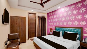 A hotel room with a bed, a chair, a desk, a ceiling fan, and a wall with a floral pattern. - Hotel O IGI Airport Mahipalpur (New Delhi)