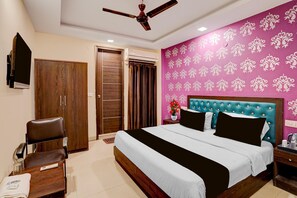 A hotel room with a bed, a chair, a desk, a ceiling fan, and a wall with a floral pattern. - Hotel O IGI Airport Mahipalpur (New Delhi)