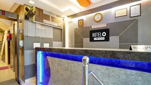A hotel reception desk with a blue illuminated feature, a clock, framed certificates, and a sign indicating check-in times. - Hotel O IGI Airport Mahipalpur (New Delhi)