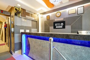 A hotel reception desk with a blue illuminated feature, a clock, framed certificates, and a sign indicating check-in times. - Hotel O IGI Airport Mahipalpur (New Delhi)
