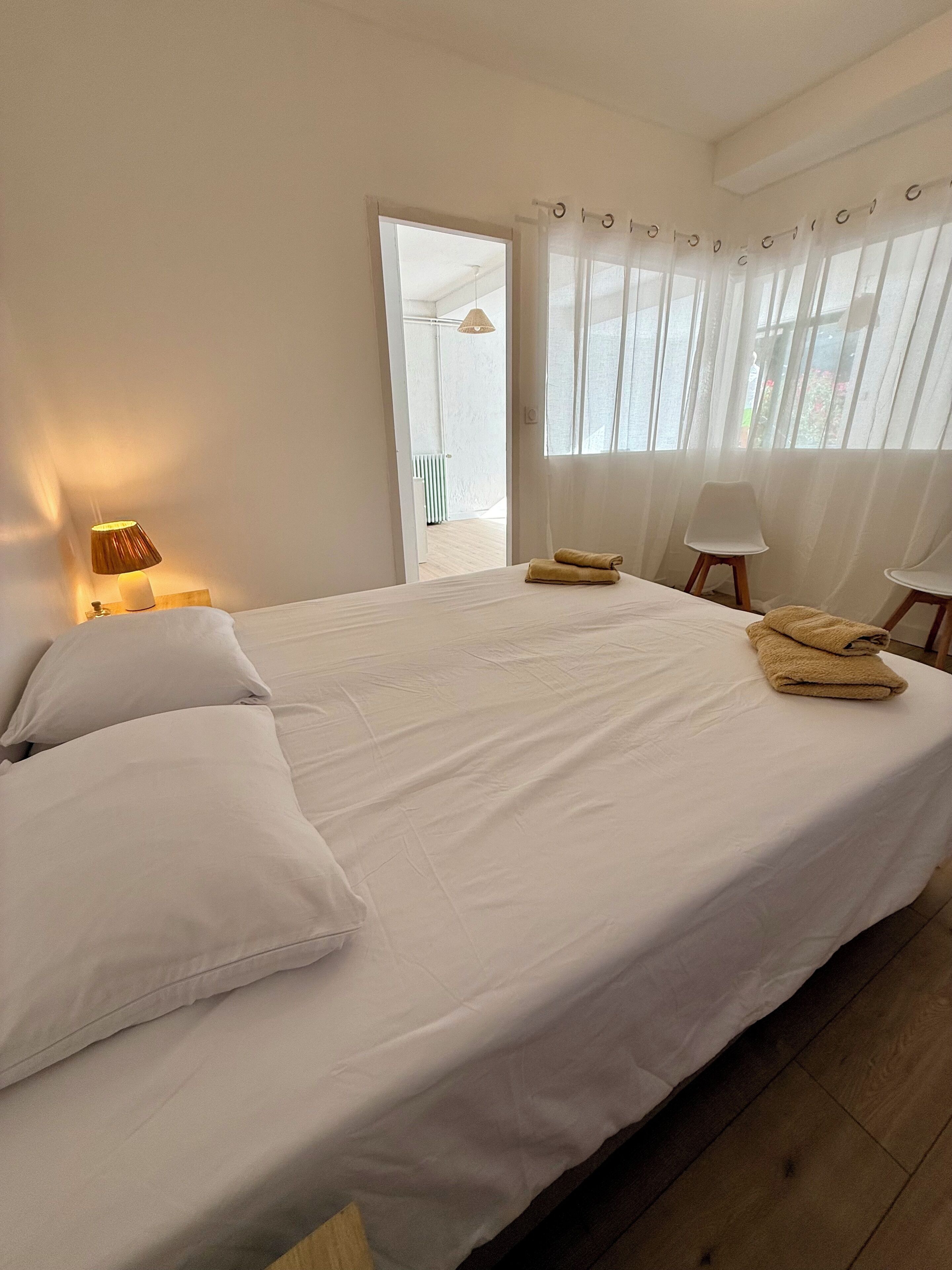 A bedroom with a bed, pillows, a lamp, a chair, and a window with curtains.