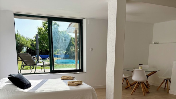 Ein modernes Schlafzimmer mit großem Fenster, einem Bett, einem Sessel und einem kleinen Tisch.