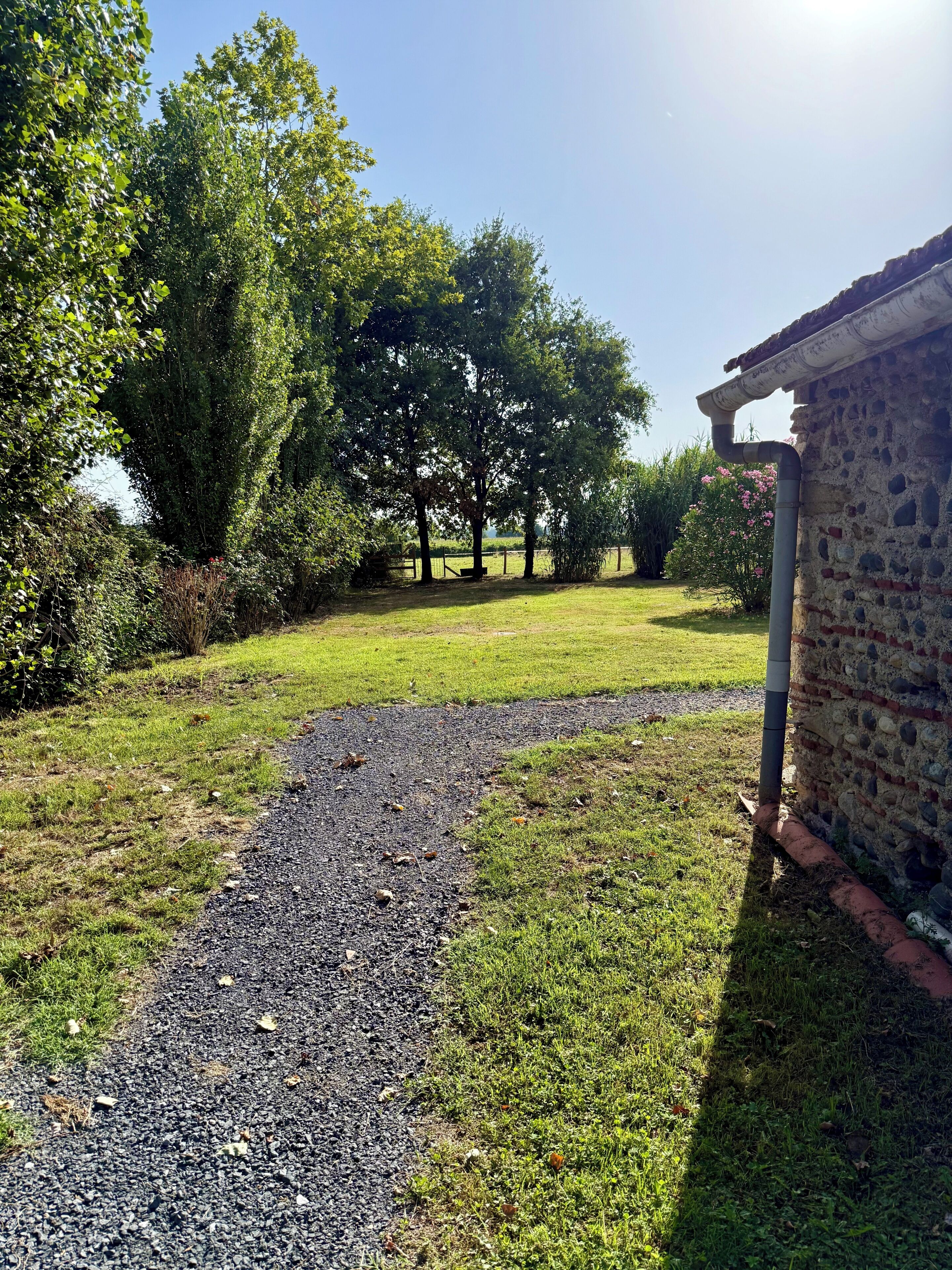 A gravel path leading to a brick building with a stone roof, surrounded by lush greenery and trees.