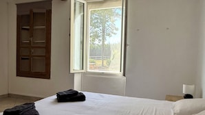 Ein Schlafzimmer mit einem großen Bett, einem Fenster mit geöffnetem Rollo, einer Holztür und einem Nachttisch mit Lampe.