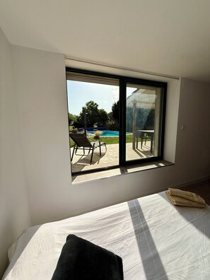 A bedroom with a large window, a bed, and a view of an outdoor swimming pool and patio furniture. - Bed and Breakfast in a renovated farmhouse, swimming pool, peaceful setting, pets welcome, naturist (Lafitole)