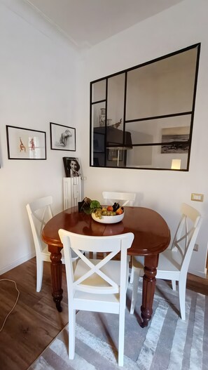A dining area with a wooden table, white chairs, a bowl of fruit, and framed artwork on the wall. - "Verdastro" Apartment with Wi-Fi and Air Conditioning Near Vatican (Rome)