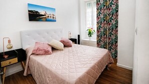 A bedroom with a bed, a nightstand, a lamp, a window with curtains, and a wall-mounted picture. - "Verdastro" Apartment with Wi-Fi and Air Conditioning Near Vatican (Rome)