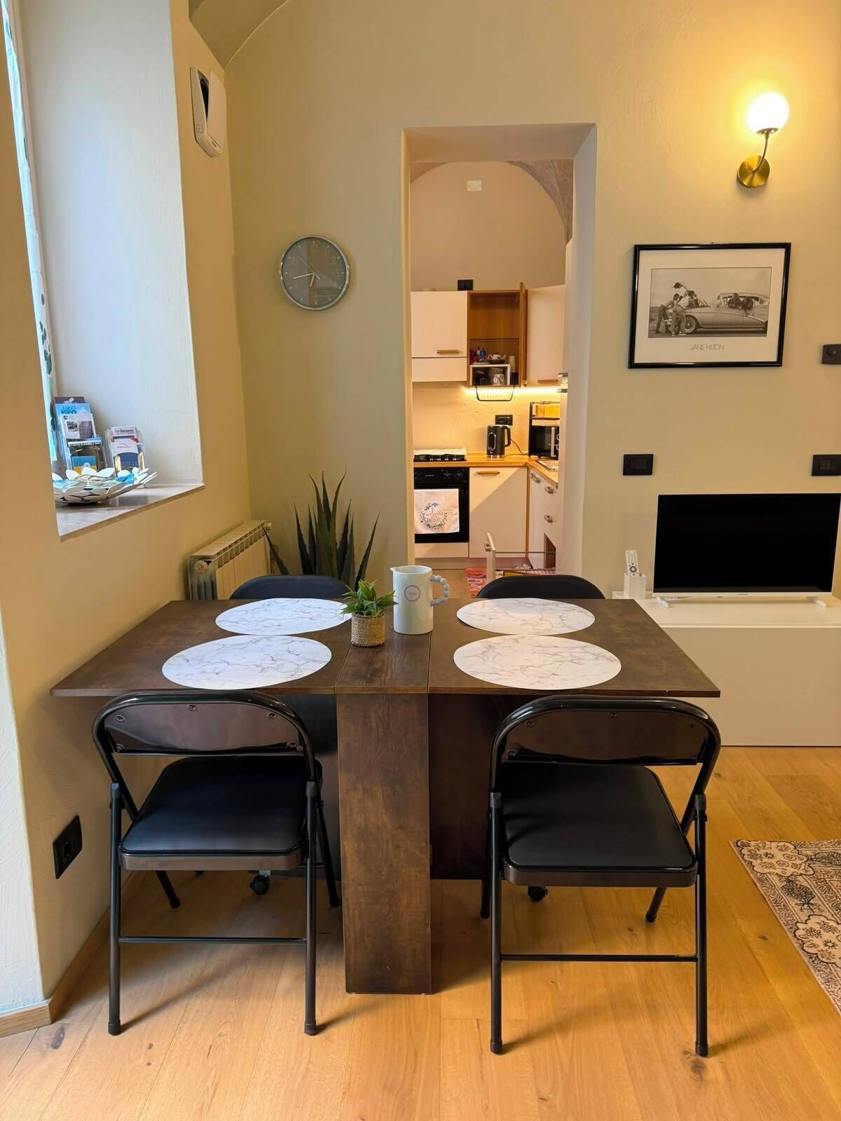 Un comedor con una mesa de madera, cuatro sillas y un reloj en la pared.