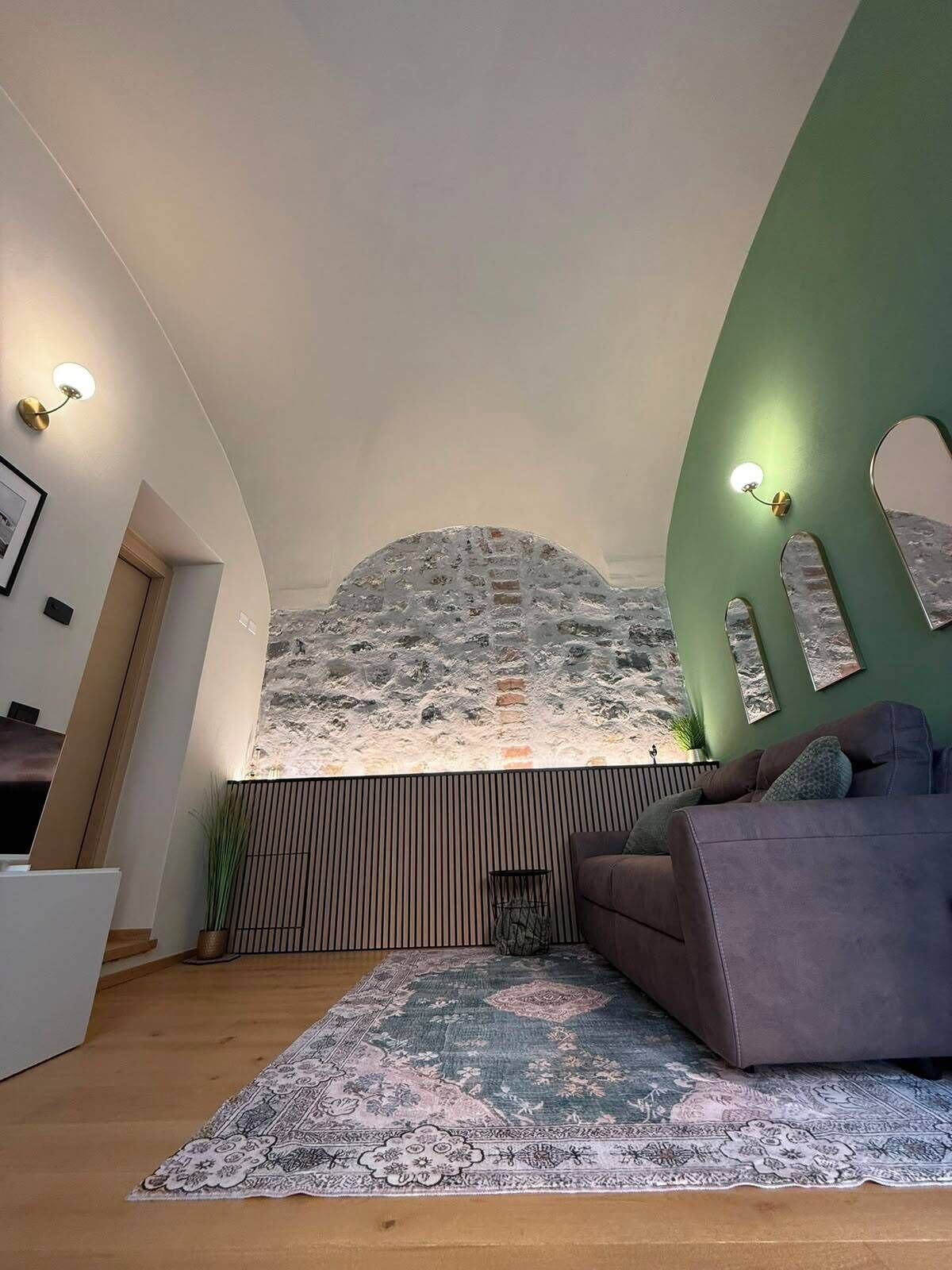 Un interior moderno con techo inclinado, pared de acento verde, alfombra estampada y sofá.