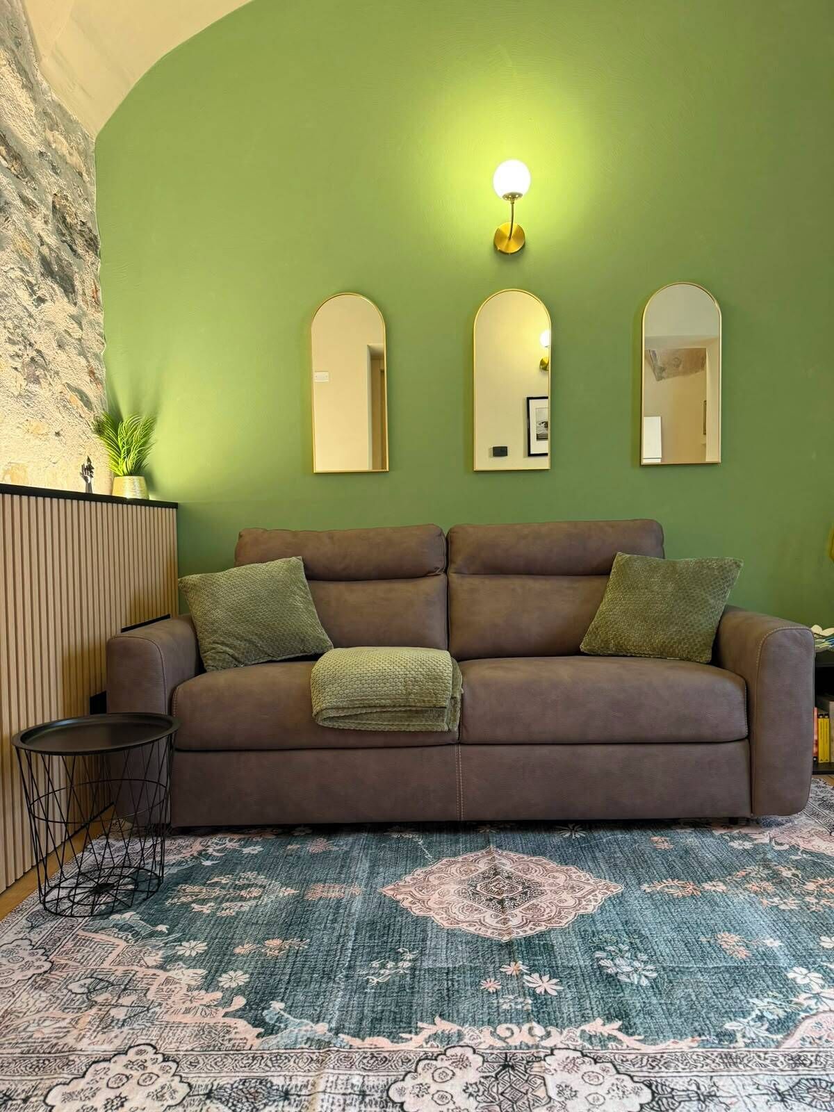 Una habitación con un sofá marrón, una pared verde y una alfombra estampada.