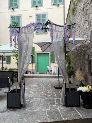 An outdoor seating area with tables and chairs, a green door, and a stone floor. - WISTERIA SECRET GARDEN ApartmentHistoric Palace&Private Courtyard (MAX 3 GUESTS) (Lovere)