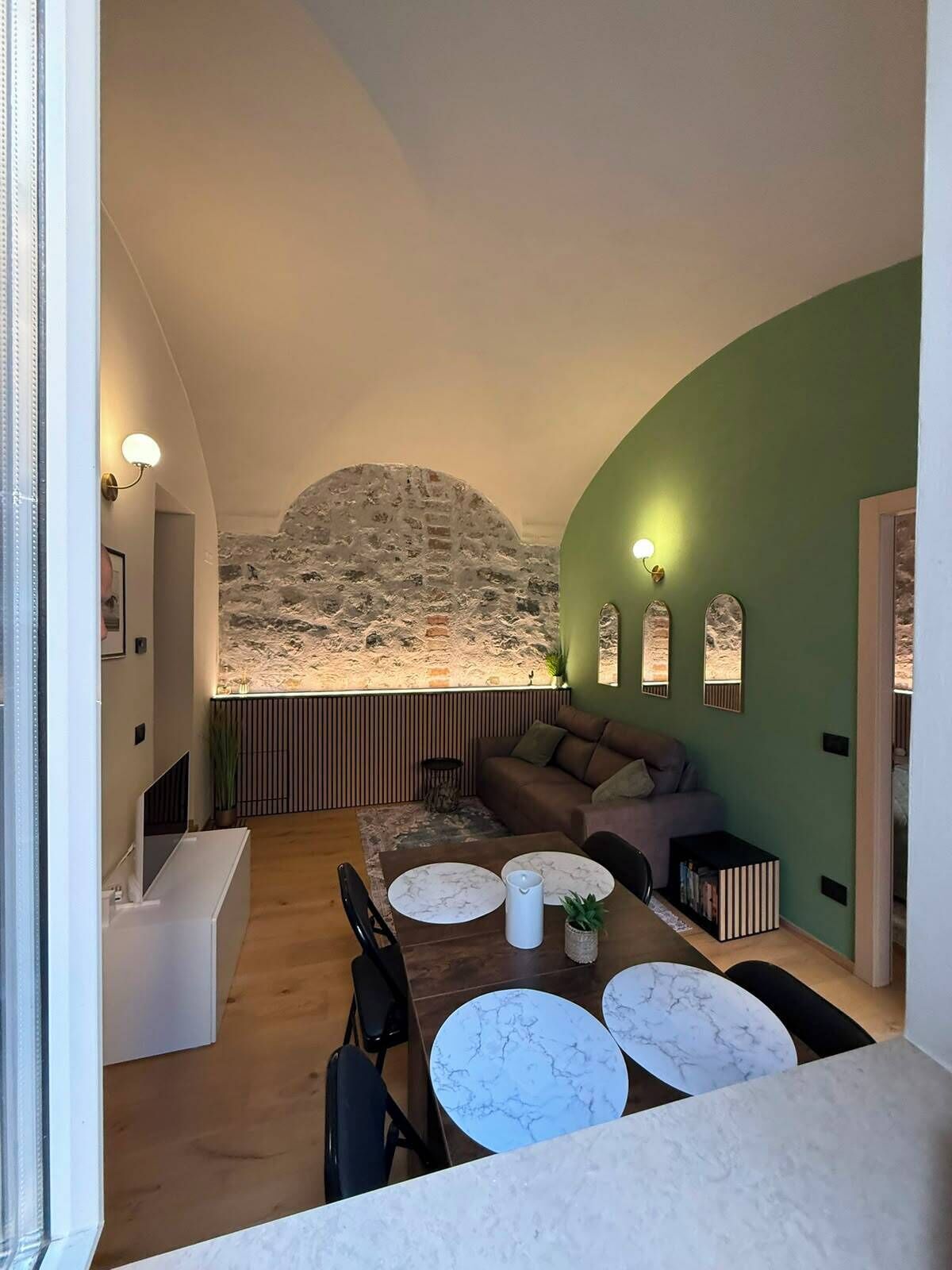 A modern interior with a stone wall feature, a dining area with a marble table, and a green accent wall.