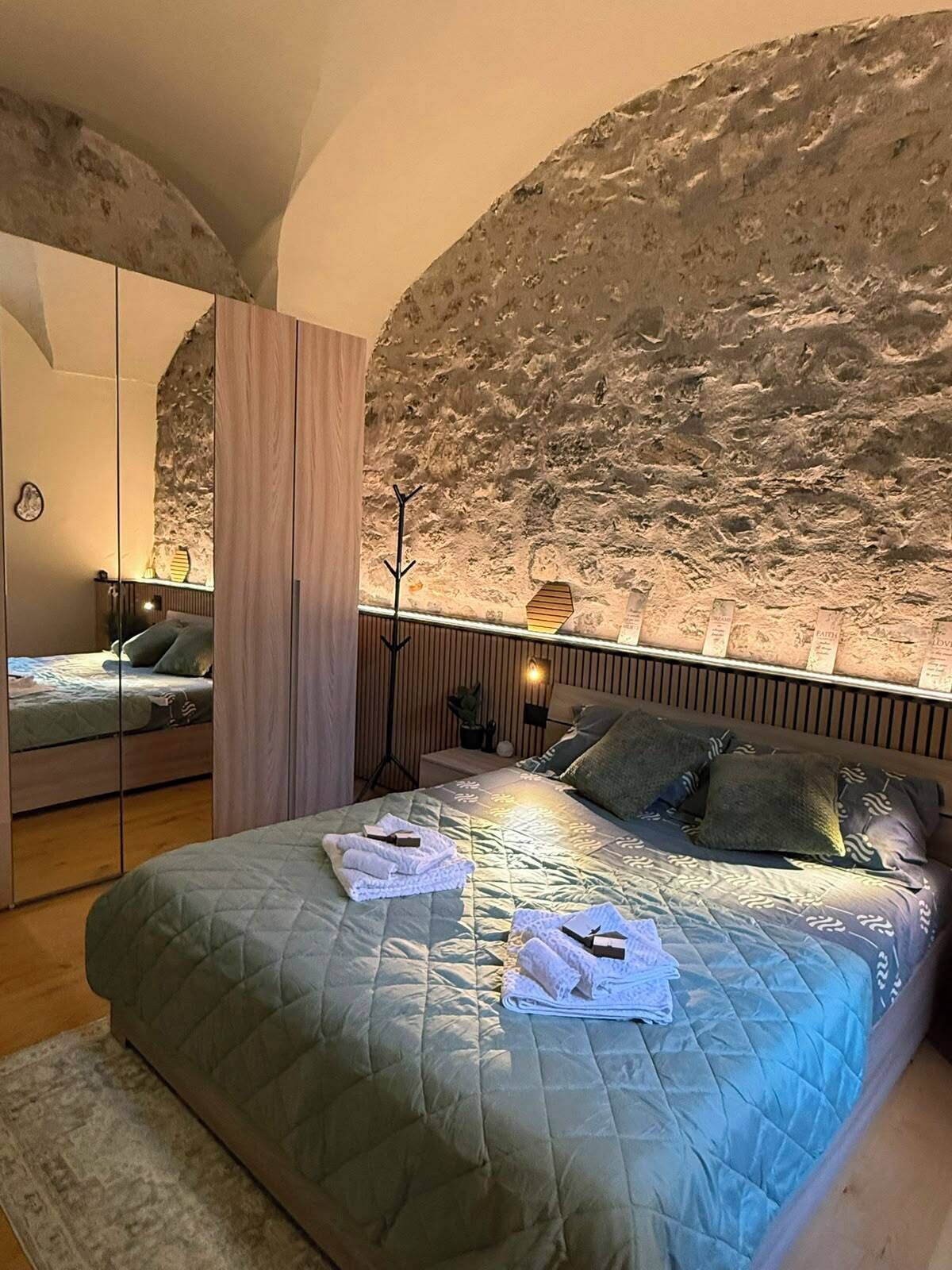 Ein Schlafzimmer mit Steinwand, einem Bett mit gesteppter Bettdecke, einem Nachttisch mit Lampe und einem Spiegel.