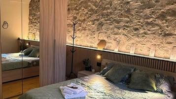 Ein Schlafzimmer mit Steinwand, einem Bett mit gesteppter Bettdecke, einem Nachttisch mit Lampe und einem Spiegel.