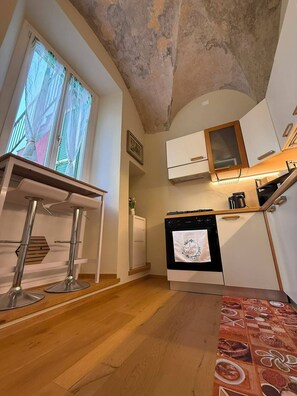 Cocina compacta con horno integrado, una mesa de comedor con taburetes de bar y una ventana con cortinas.