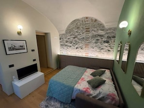 A bedroom with a stone wall, a bed with a floral duvet, a mounted TV, and a framed picture on the wall.