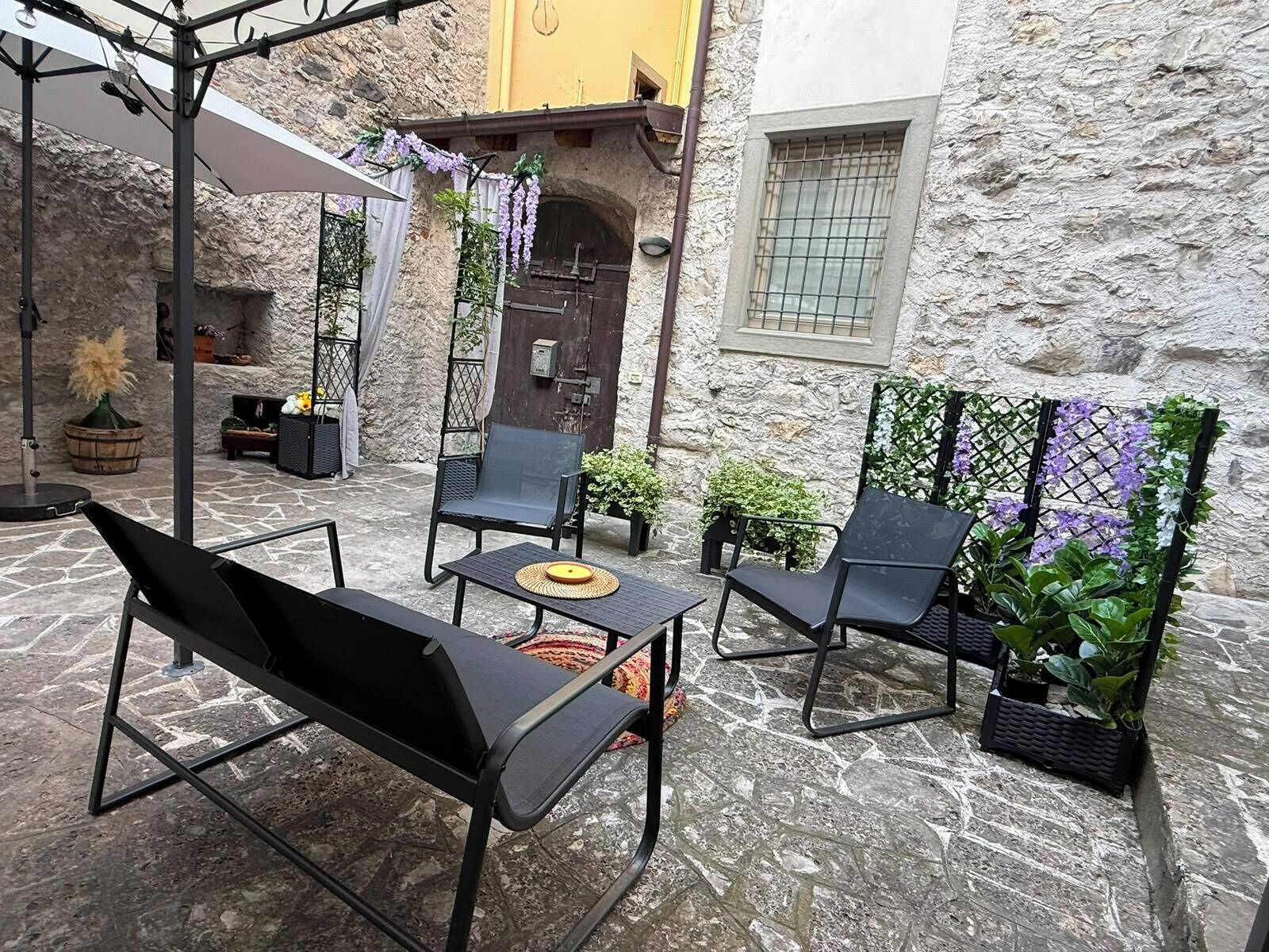 Een terras met metalen stoelen en tafels, omgeven door stenen muren en potplanten.