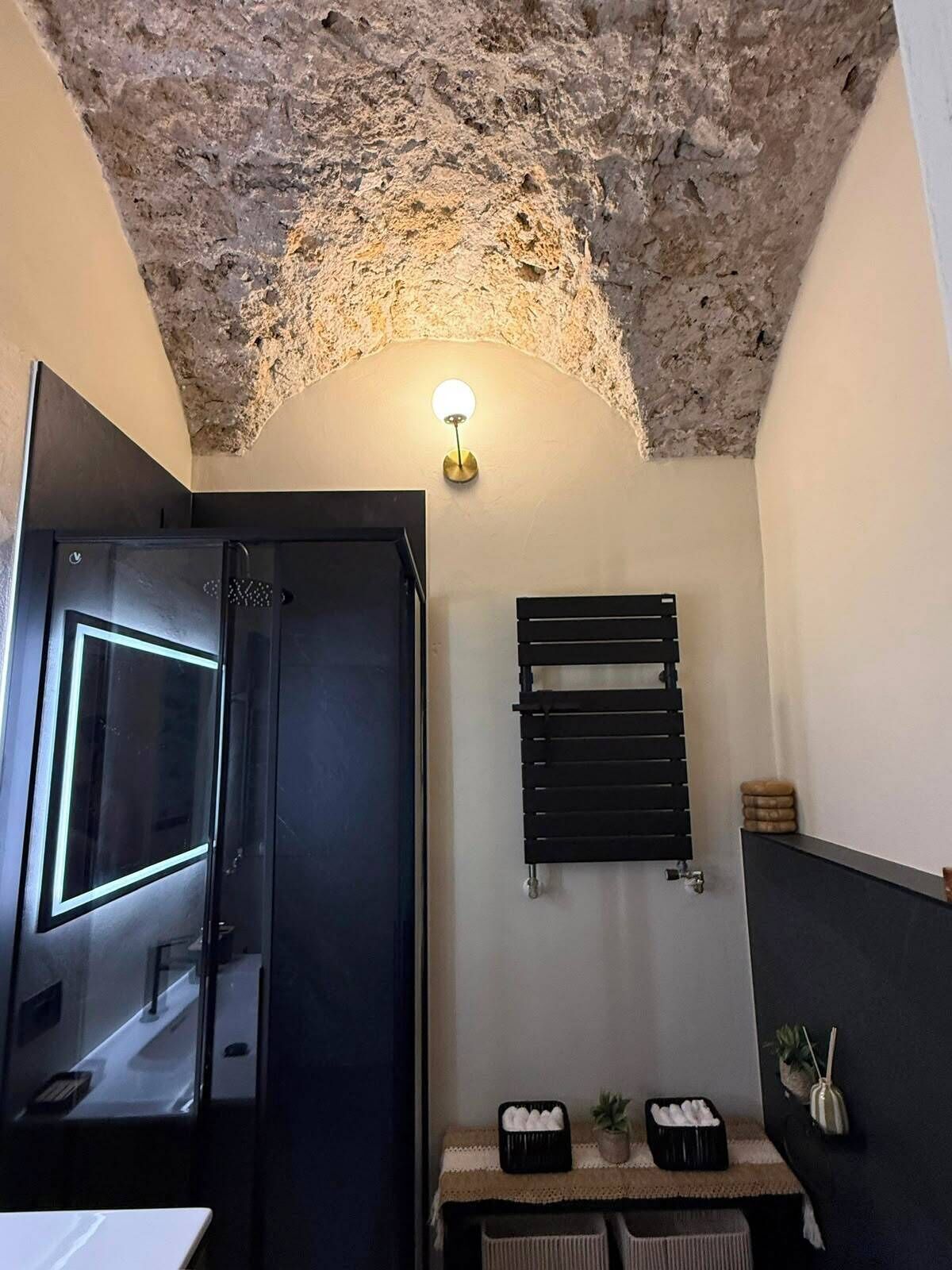 A bathroom with a rough-textured ceiling, a wall-mounted towel rack, a small table with toiletries, and a door with a frosted glass panel.