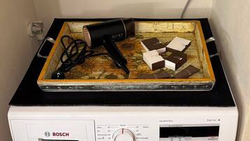 Un lave-linge Bosch avec un étendoir placé sur le dessus, une prise de courant et une étagère sur laquelle se trouvent une plante, une pelote de laine et un paquet de lessive.