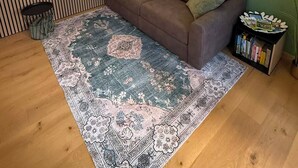 Ett rum med en grön vägg, en brun soffa, en mönstrad matta och en bokhylla.