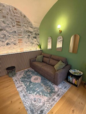A room with a green wall, a brown sofa, a patterned rug, and a bookshelf. - WISTERIA SECRET GARDEN ApartmentHistoric Palace&Private Courtyard (MAX 3 GUESTS) (Lovere)