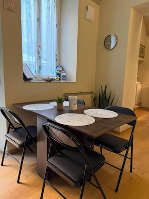 A dining area with a marble-top table, black chairs, a potted plant, and a window with curtains.
