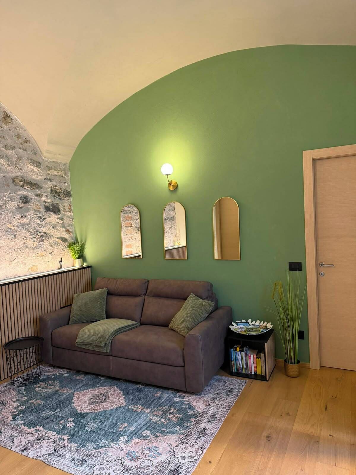 Un salón con un sofá marrón, un tapete estampado, una pared verde y una puerta de madera.