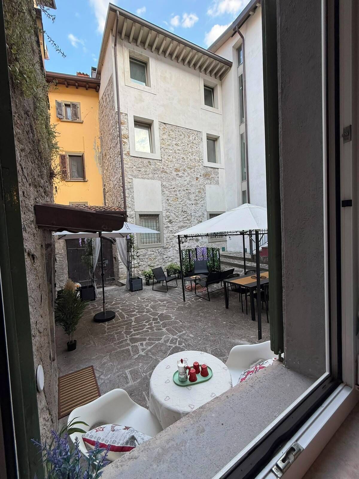 Un patio con mobiliario exterior, suelo de piedra y vistas a edificios vecinos.
