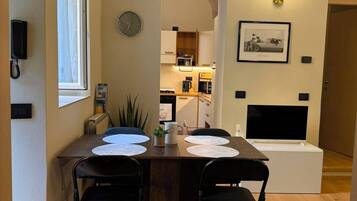 A dining area with a wooden table, four chairs, a clock, and a framed picture on the wall.