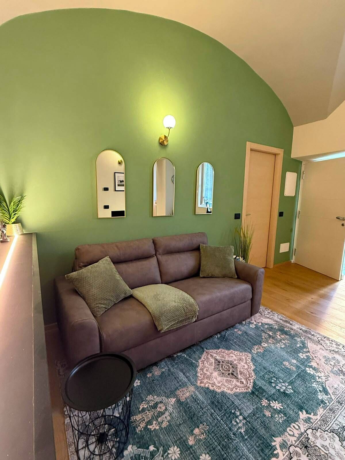 Ein Wohnzimmer mit braunem Sofa, einem gemusterten Teppich und drei Wandspiegeln.