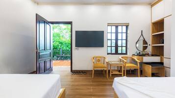 A hotel room with two beds, a desk with a chair, a TV, and a window with a view of greenery.