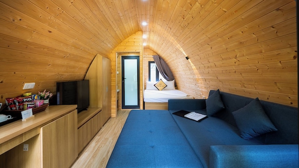 Habitación pequeña con techo de madera, una cama, un sofá azul y un televisor pequeño sobre una mesa de madera.