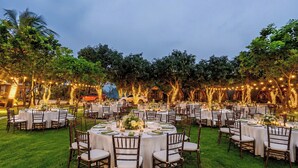 Un espacio exterior para comer con mesas y sillas redondas, rodeado de árboles y luces colgantes.