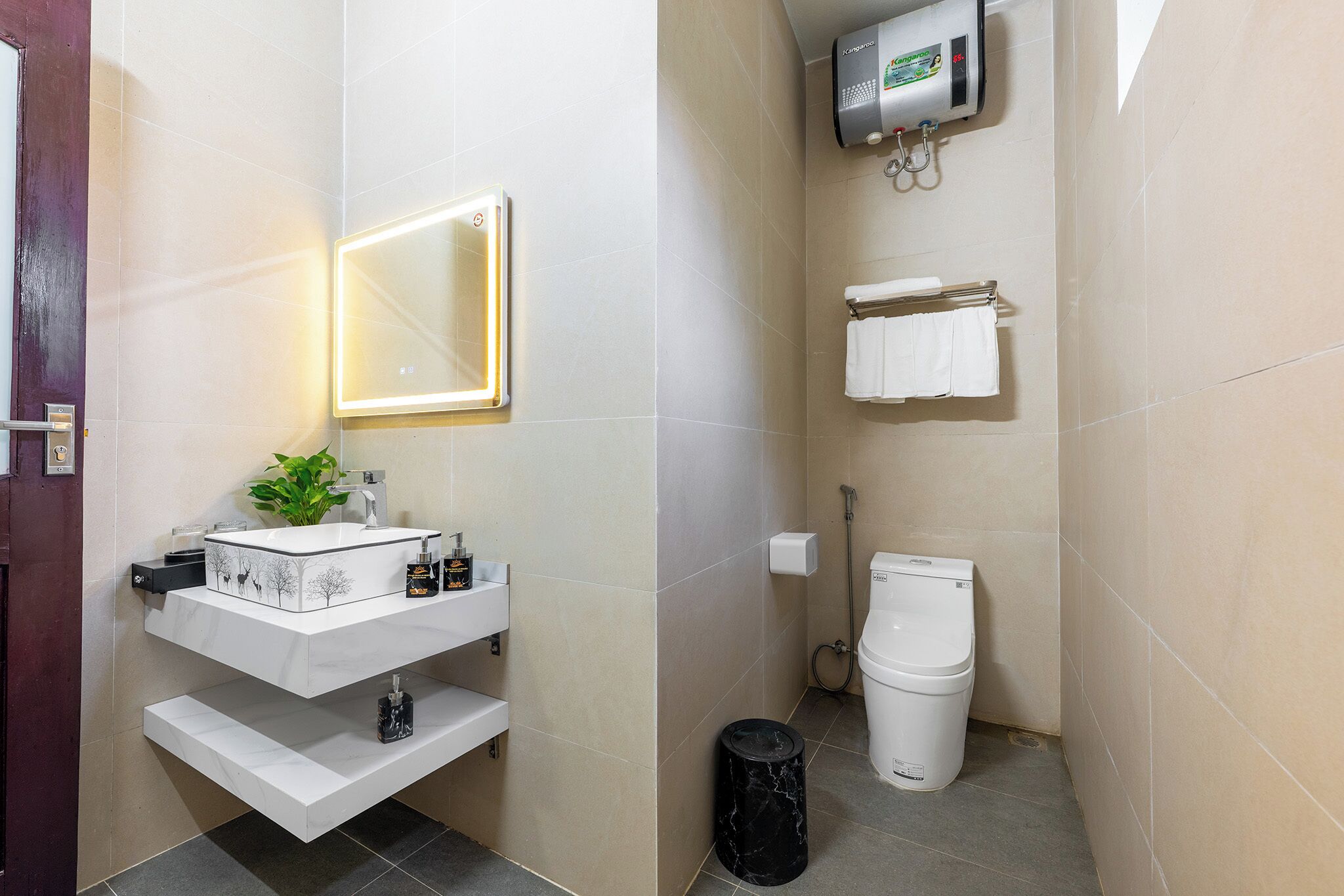 Casa de banho compacta com uma sanita, lavatório branco, espelho e um pequeno contentor de lixo.
