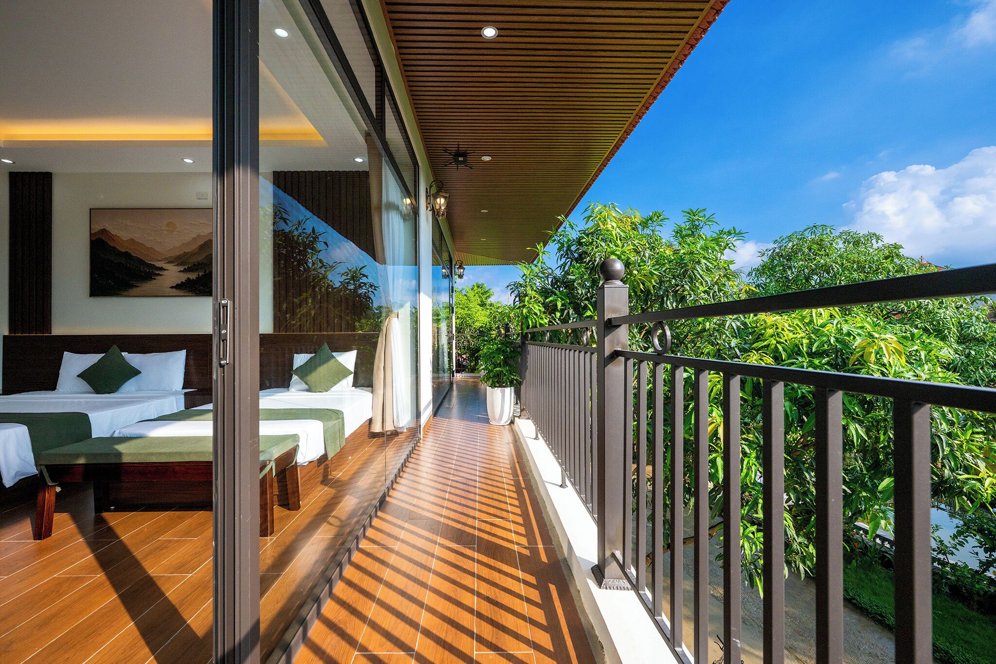 A balcony with a wooden floor, a metal railing, and a view of greenery.