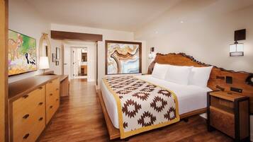 A hotel room with a bed, wooden furniture, a painting, and a view into the hallway.