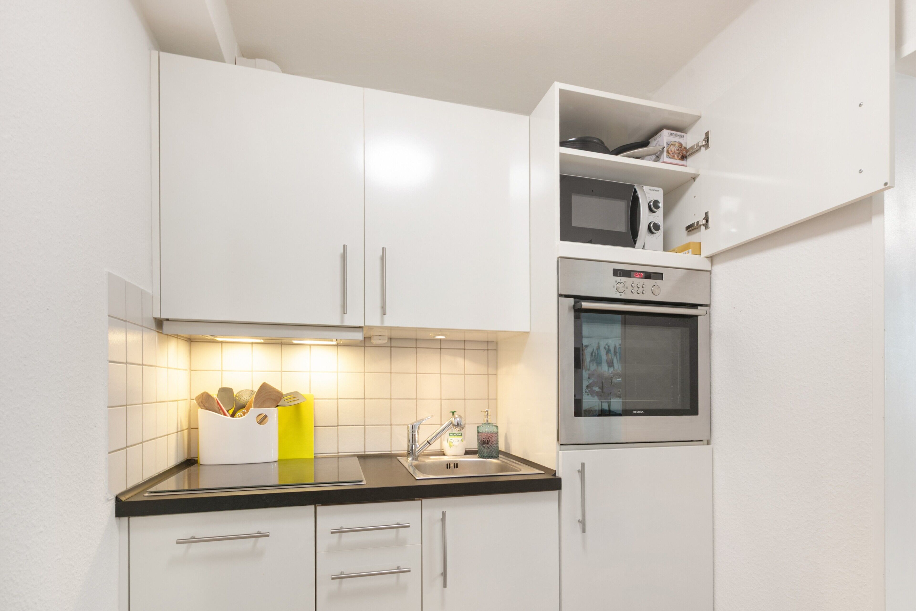 Eine kleine Küche mit weißen Schränken, einer Mikrowelle und einem Backofen.