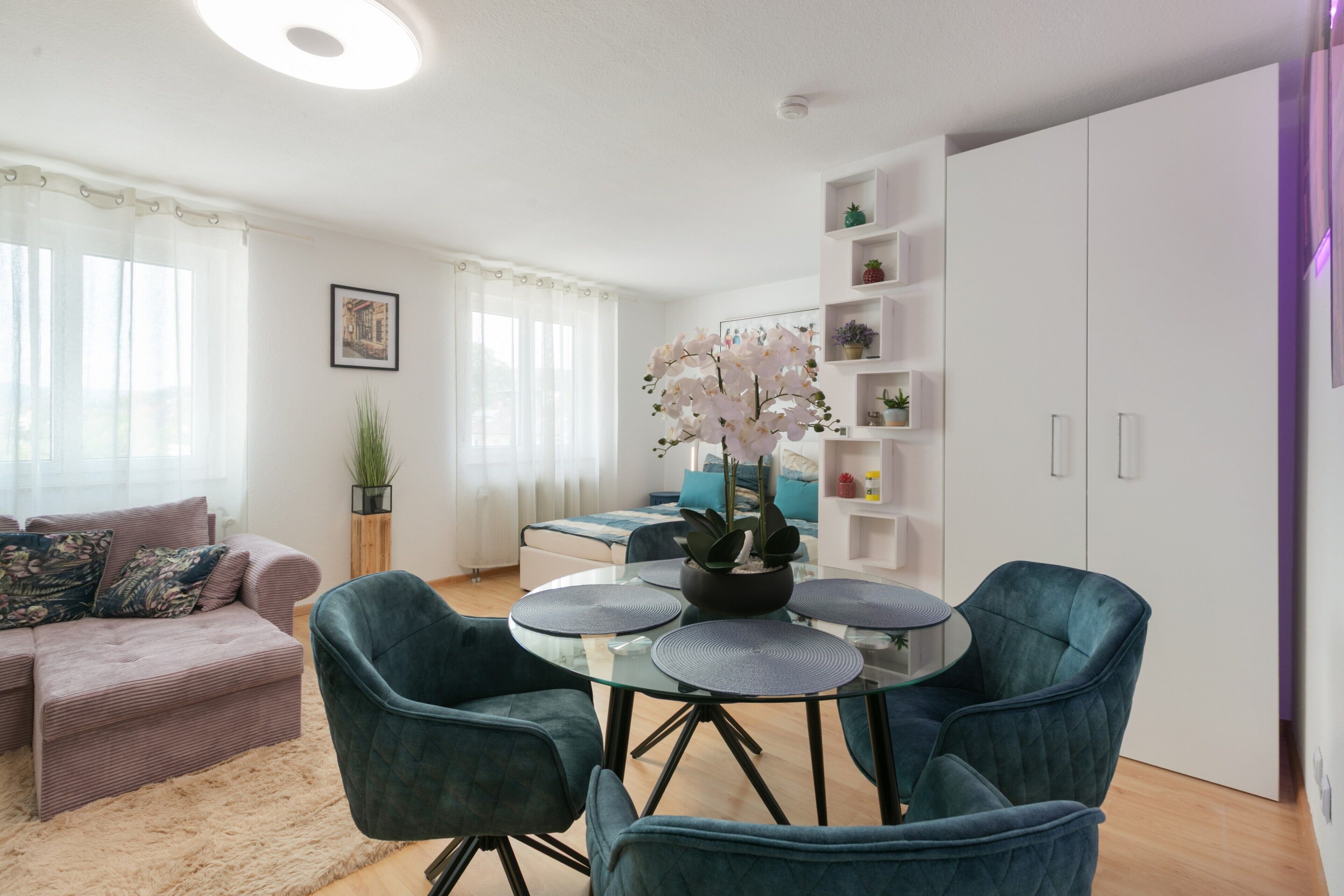 Ein modernes Wohnzimmer mit einer Couch, einem Esstisch mit Stühlen und einer Küchenzeile mit Schränken und Regalen.