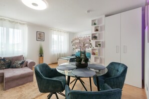 A modern living room with a sofa, a dining table with chairs, and a kitchen area with cabinets and a shelf.