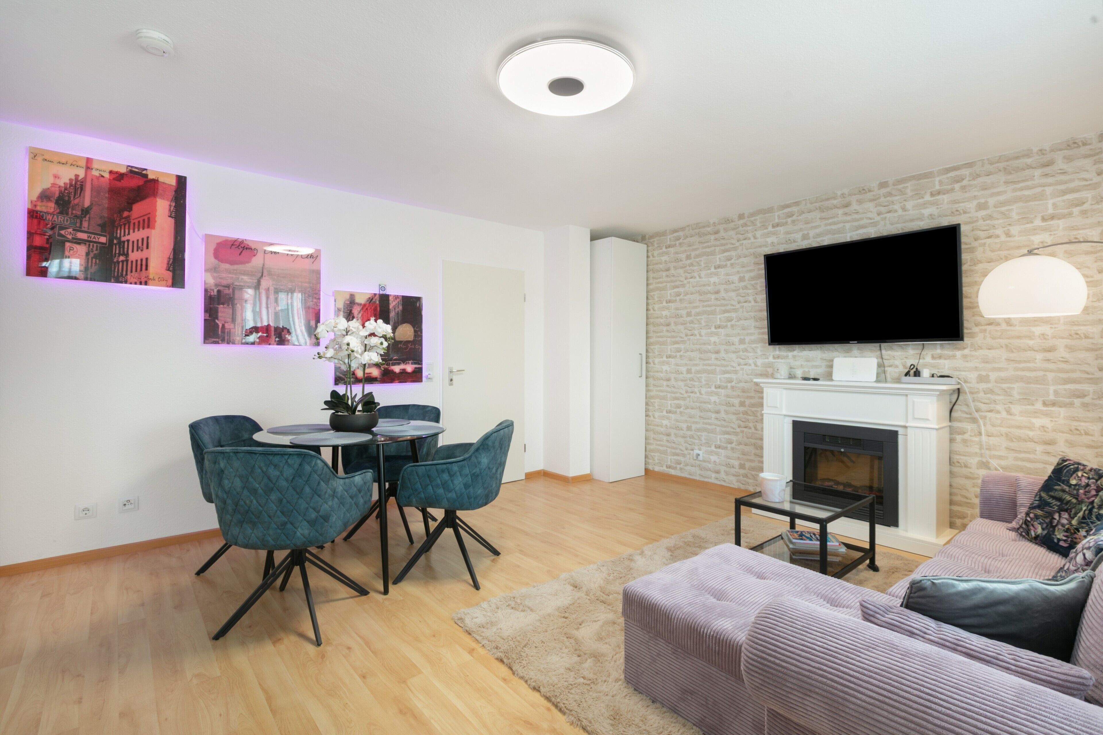 Ein modernes Wohnzimmer mit Kamin, Flachbildfernseher und Essbereich mit Stühlen und Tisch.