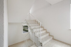 A staircase with a metal railing, a small window, and a plain wall.