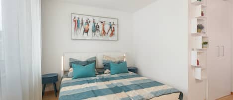 A bedroom with a bed, a bedside table, a nightstand, a wall-mounted shelf with plants, and a painting.