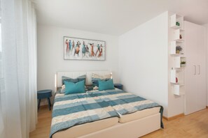 Un dormitori amb un llit, una taula de nit, una estanteria penjada a la paret amb plantes i un quadre.