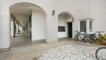 Une allée couverte, dont le sol est en pierre, mène à l’entrée d’un bâtiment devant lequel est garé un vélo.