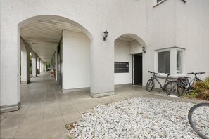 A covered walkway with stone flooring, leading to a building entrance with a bicycle parked outside.