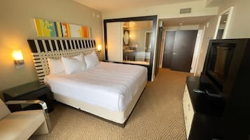 Hotelkamer met groot bed, bureau, stoel, televisie en zichtbare badkamer door een glazen deur.