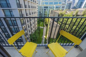 Ein Balkon mit gelben Stühlen, mit Blick auf eine Stadtlandschaft mit modernen Gebäuden und einem grünen Park.