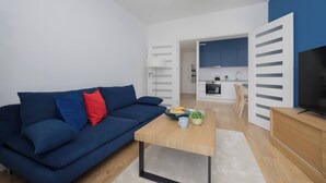 A modern living room with a blue sofa, a coffee table, and a TV on a wooden stand. - Stylish Apartment with Air Conditioning | Parking | Close to the City Centre (Warszawa)